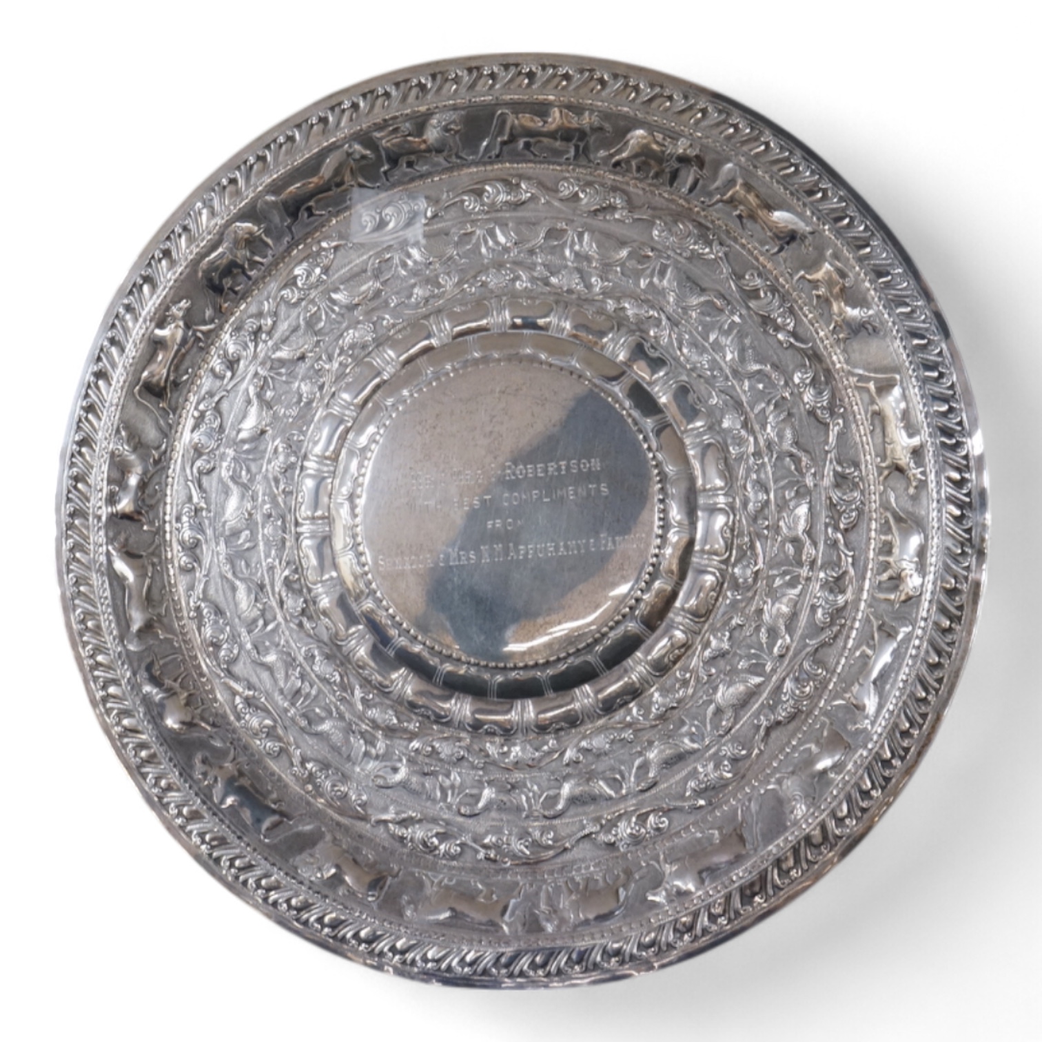 A mid 20th century Ceylonese white metal (tests as silver) presentation charger, embossed with animals. birds and foliage, with presentation inscription, makers mark HB, diameter 31.5cm, together with an associated circu